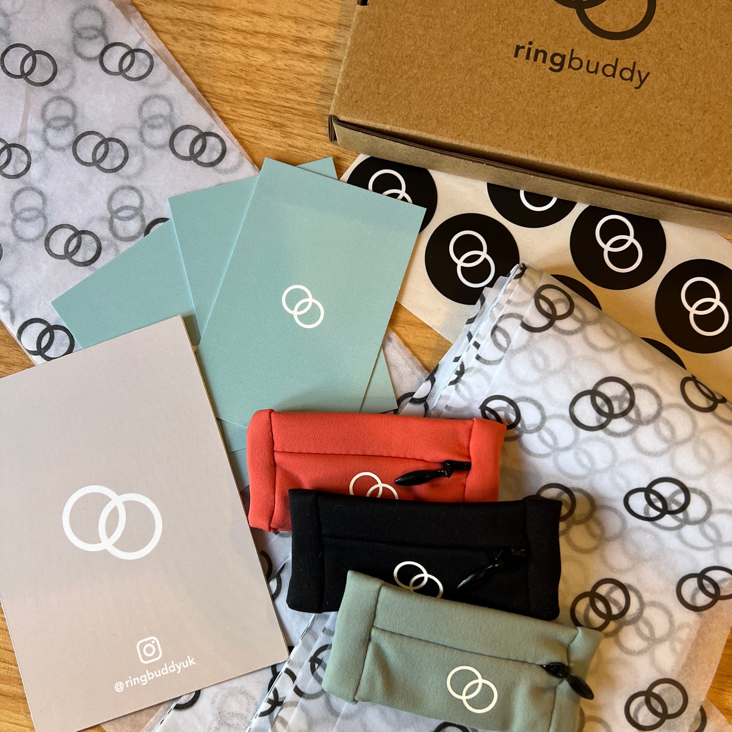 Ringbuddy product packaging with colorful pouches and branded boxes on a patterned surface.